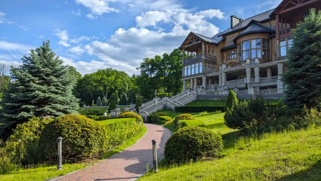 Stunning wooden manor surrounded by well-manicured gardens and vibrant trees under a clear blue sky.